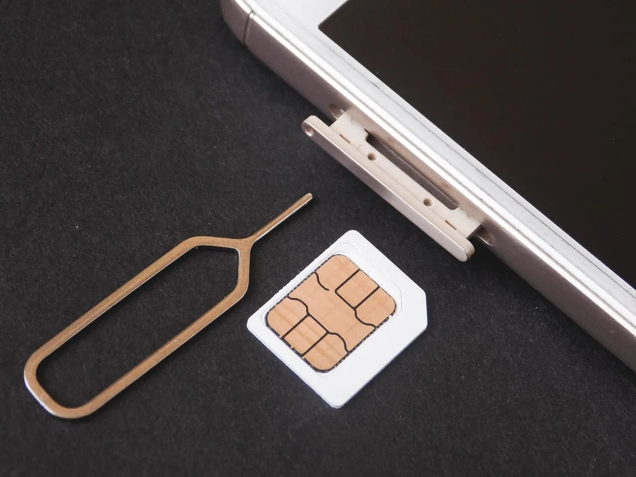 Eine Nano-SIM-Karte und eine Auswurfnadel liegen neben dem geöffneten Kartenschacht eines Smartphones