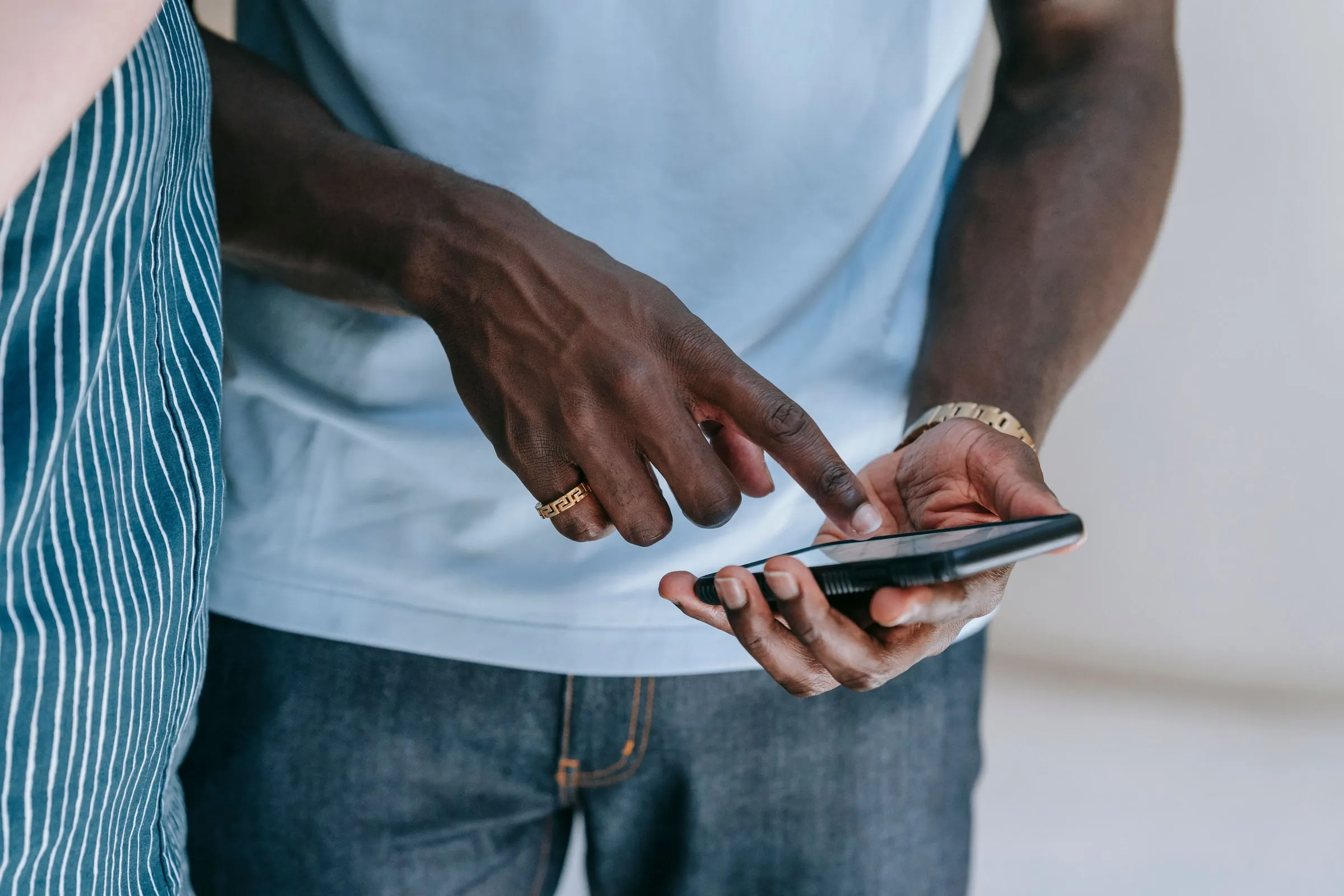 Eine Hand zeigt auf das Smartphone in der Hand eines anderen Menschen, Gesichter sind nicht im Bild