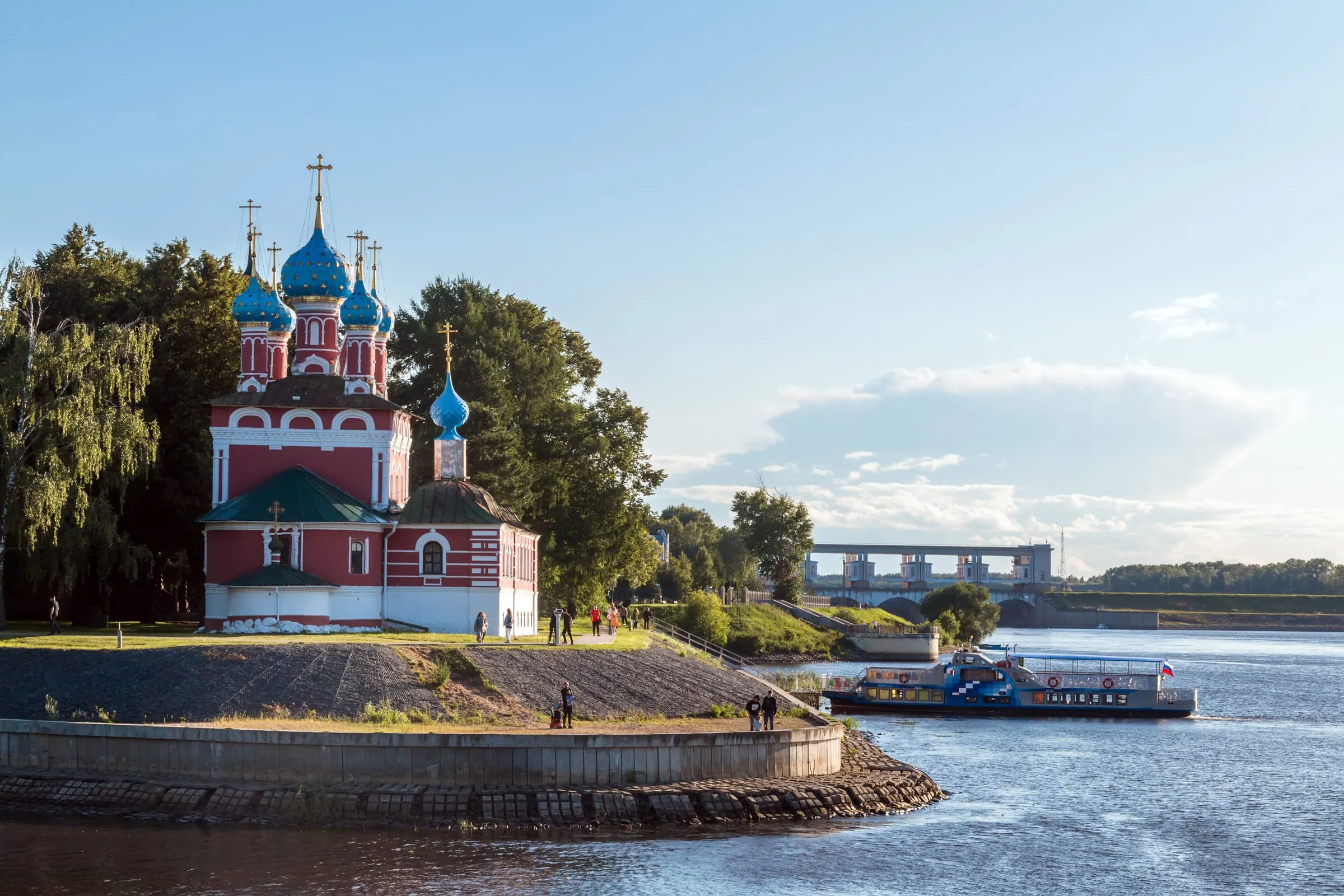 Die blutrote Kirche Dimitri auf dem Blut mit blauen Sternenkuppeln am Wolga-Ufer von Uglitsch, dahinter ein Ausflugsschiff und die Schleuse des Stausees