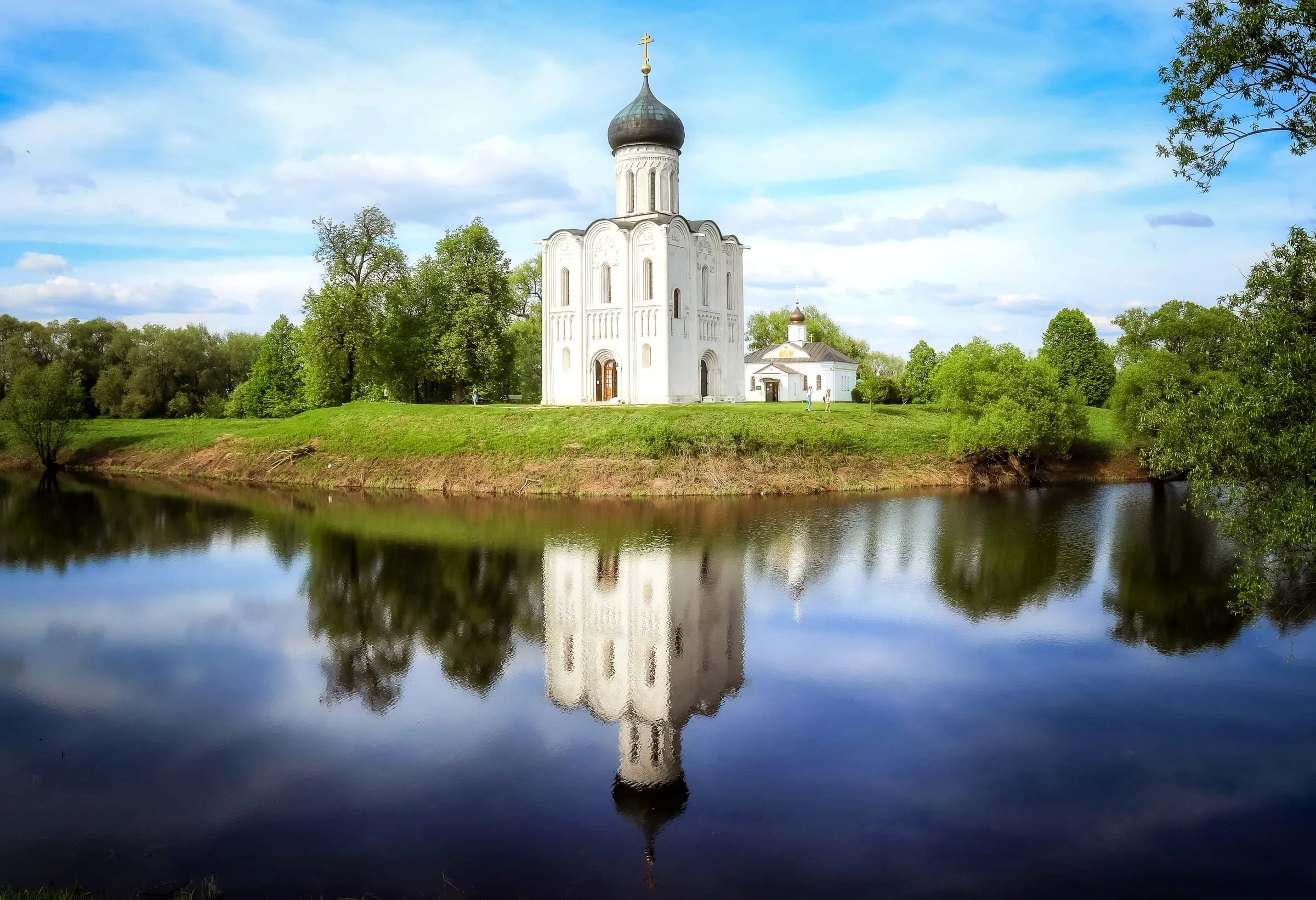 Die Mariä-Schutz-Kirche an der Nerl bei Bogoljubowo auf ihrem Hügel, gespiegelt im stillen Altwasser davor
